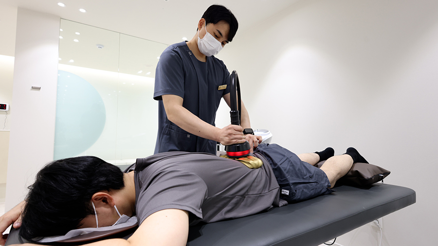 물리치료사가 엎드린 환자의 허리를 치료 기기로 치료하는 모습